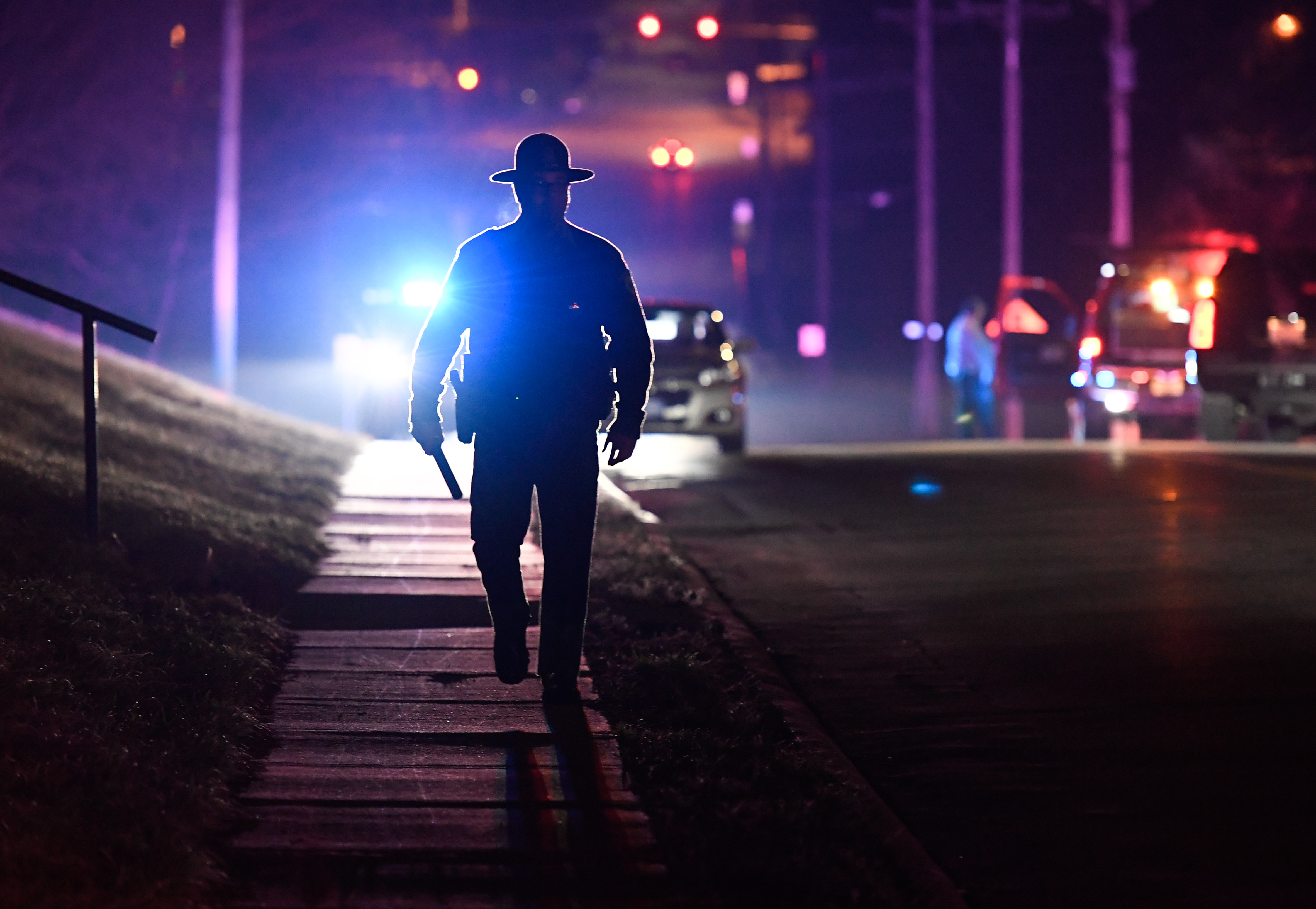 An Illinois State Trooper is silhouetted against the emergency lights while walking up 1st Street, in Coal Valley, near the scene of a reported shooting Wednesday March 11, 2020.
