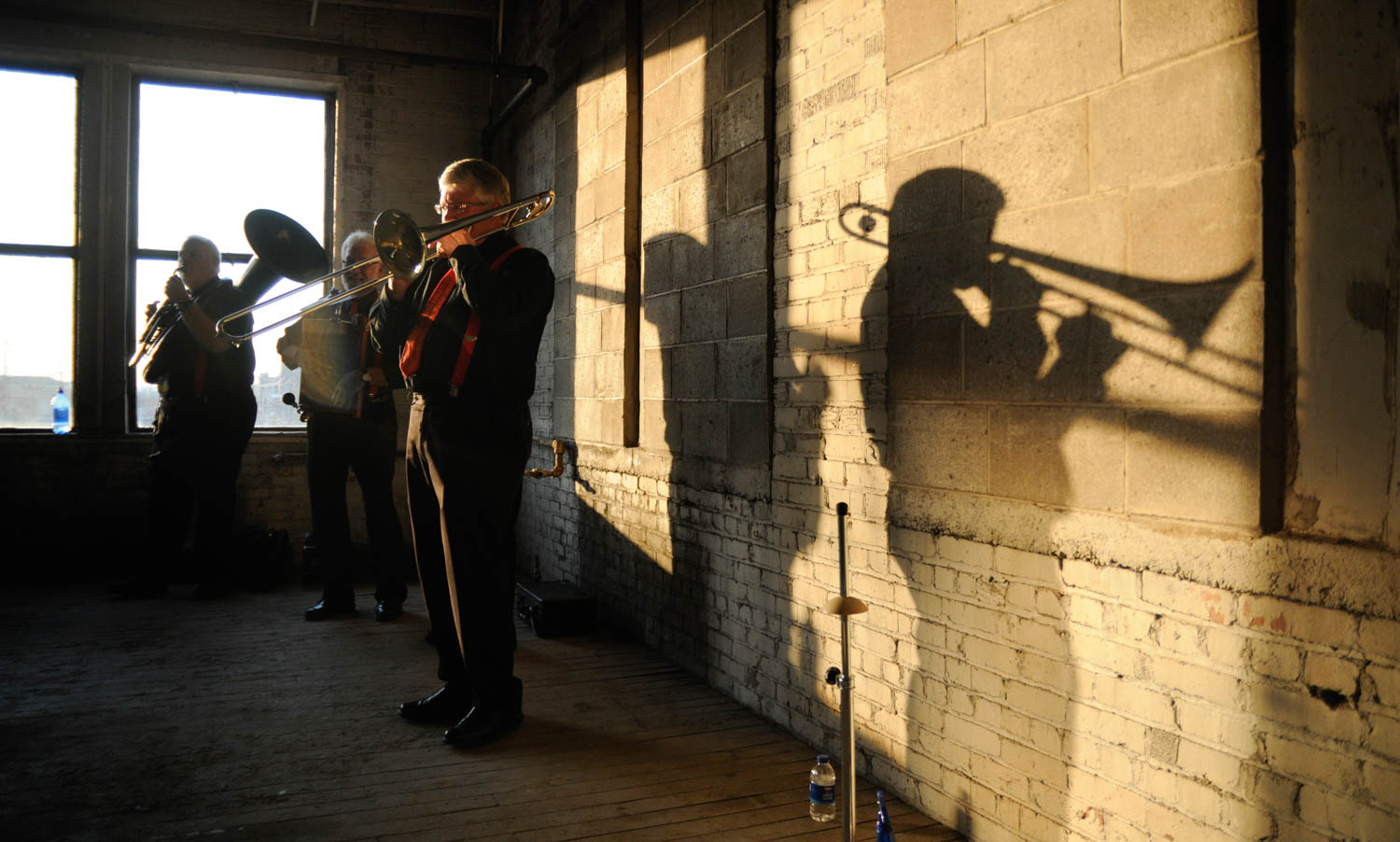'Jinosterrifics' trombonist Jim Lee casts long shadow while he and his bandmates entertain the crowd at Thursday's ceremonial groundbreaking for the Jackson Square development late Wednesday afternoon in Rock Island. The Jackson Square project will redevelop the old Illinois Oil Products building, 321 24th Street, into 30 residential rental units and 3,700 square feet for future commercial space. (Todd Mizener - Dispatch/Argus)